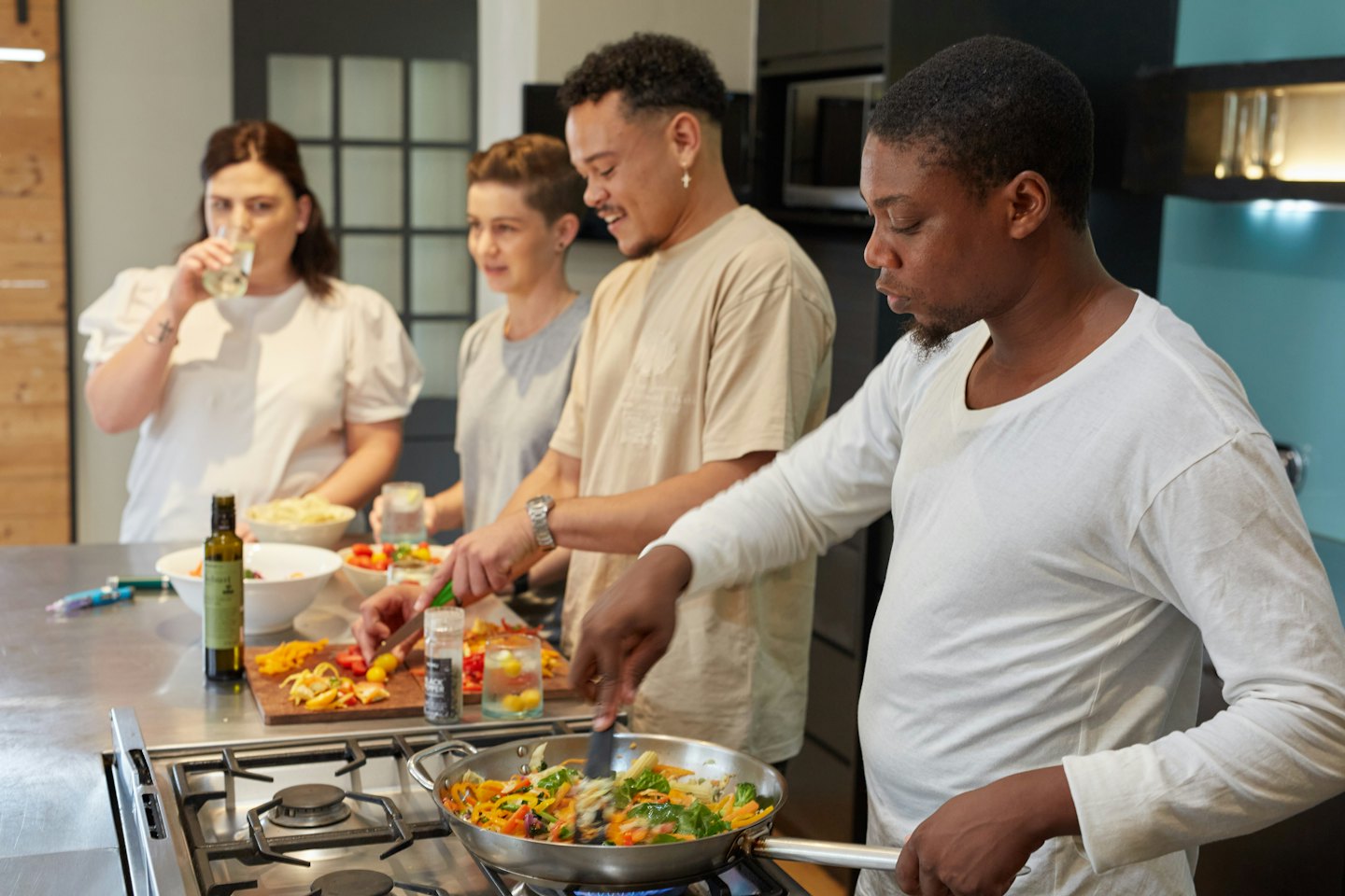 Vier Erwachsene kochen gemeinsam in einer modernen, hellen Küche.