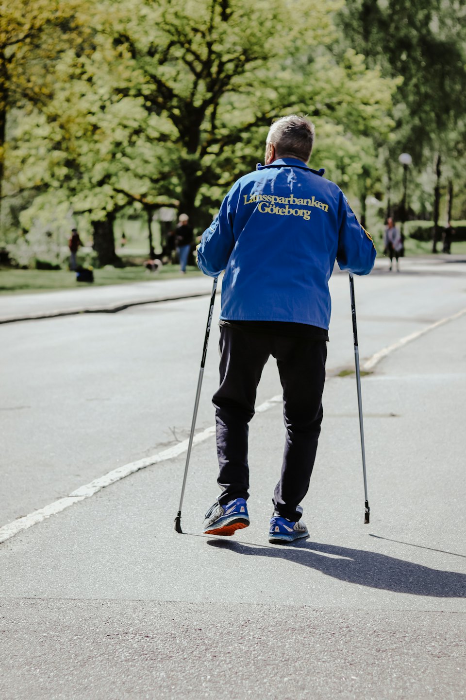 Person beim Nordic Walking auf einem Weg durch Bäume.